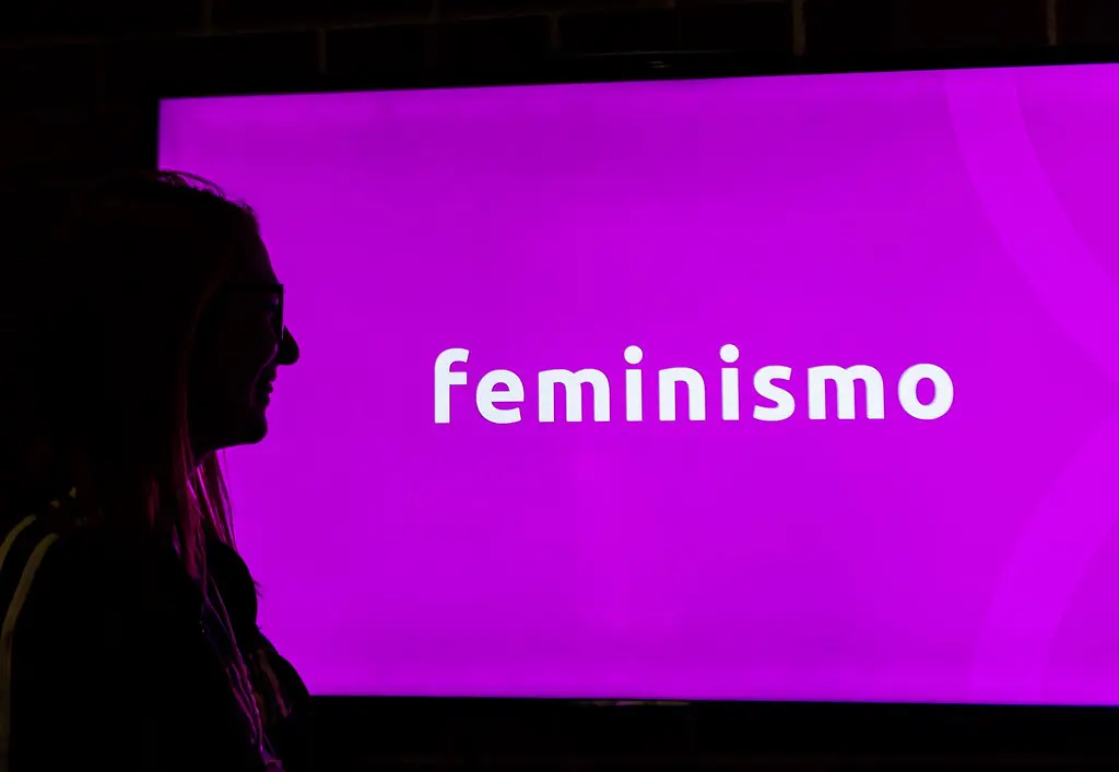 Espectadora observa tela rosa com a palavra feminismo